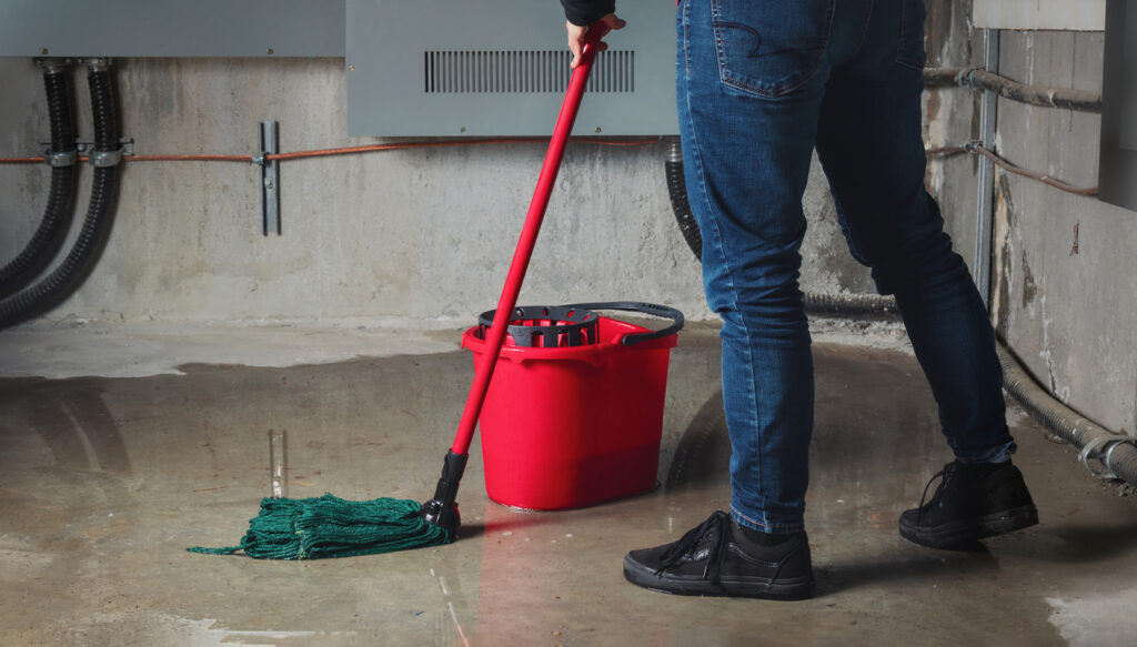 Water damage from rain, snowmelt or pipe burst coming from multiple cracks and leaks in concrete wall and ceiling being mopped up by a person