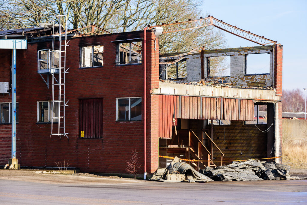 A small industrial building has burnt down - the roof is gone and some of the metal roof beams has been bent by the heat